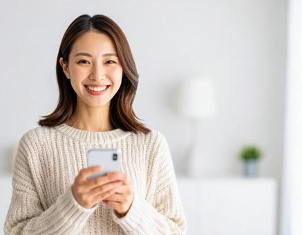 室内でスマートフォンを持つ笑顔の女性 室内でスマートフォンを持つ笑顔の女性の写真
