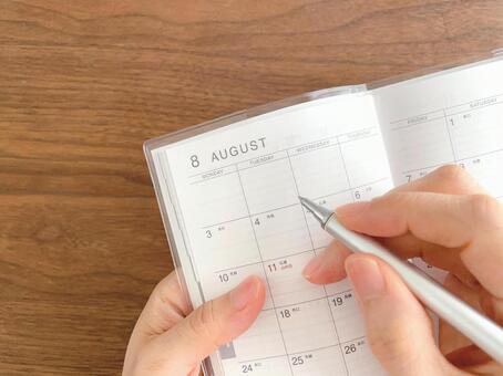 8月のスケジュール帳に記入する女性の手元 スケジュール帳,書く,手の写真素材