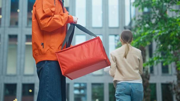 屋外でピザのデリバリーを受け取って帰る女性と保温ピザバッグを持つ配達員の男性 配達,フードデリバリー,デリバリーの写真素材