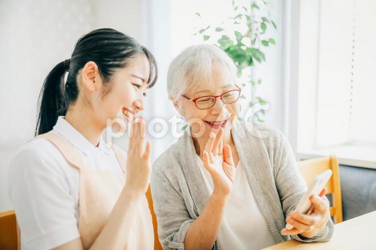 スマホを使う高齢者と女性スタッフ（テレビ電話） 高齢者,スマホ,テレビ電話の写真素材