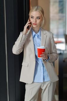 オフィスでコーヒー片手に電話している女性 ビジネスウーマン,ビジネス,女性の写真素材