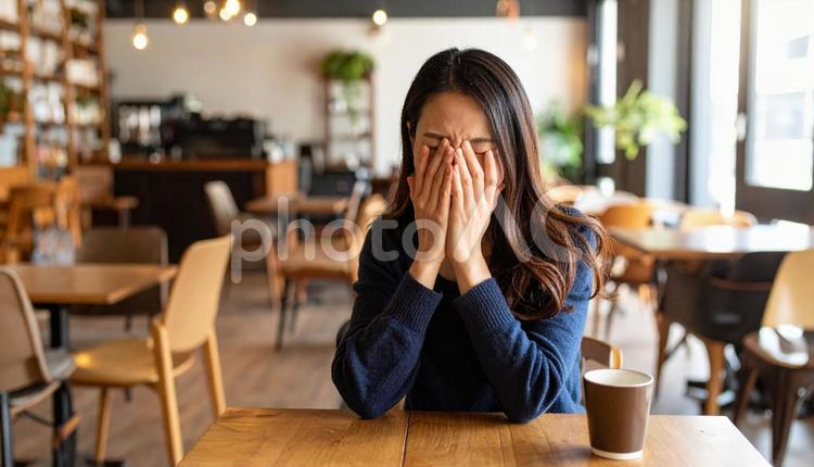 カフェで感情を押し殺すように顔を覆う女性 悲しみ,涙,落ち込むの写真素材