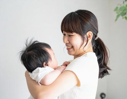 赤ちゃんを抱いて微笑んでいる若いお母さん 赤ちゃんを抱いて微笑んでいる若いお母さんの写真