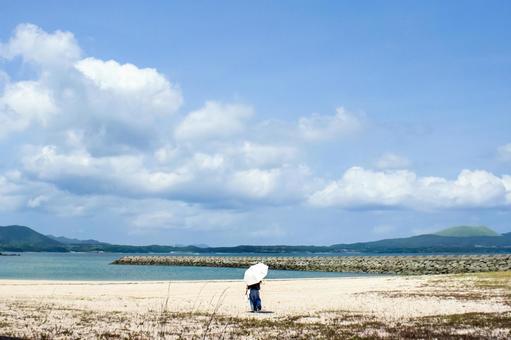 <素材>夏の浜辺を一人散策する日傘の女性 <素材>夏の浜辺を一人散策する日傘の女性の写真