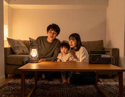 災害で停電の夜にラジオで情報収集する家族の写真