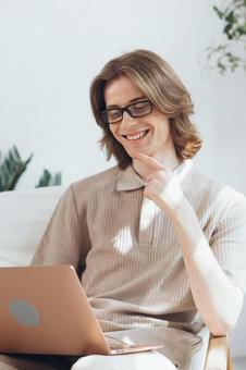 リビングで膝の上にノートパソコン乗せて使う笑顔の若い男性 男性,外国人,欧米人の写真素材