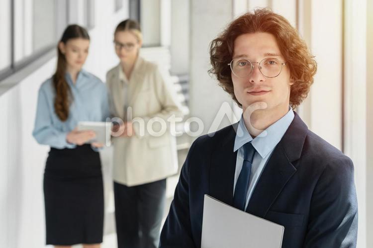 オフィスの廊下でタブレットを見て話している女性たちとカメラ目線の男性 ビジネス,グループ,ビジネスマンの写真素材