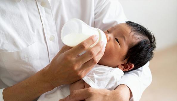 椅子に座り赤ちゃんに哺乳瓶で授乳する父親 椅子に座り赤ちゃんに哺乳瓶で授乳する父親の写真