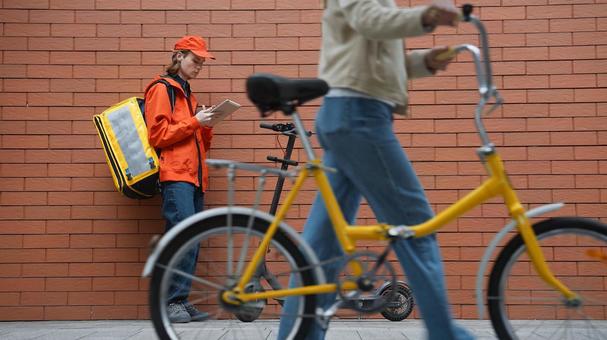 タブレットを使うフードデリバリーの男性と自転車を押して歩く女性通行人 配達,フードデリバリー,デリバリーの写真素材