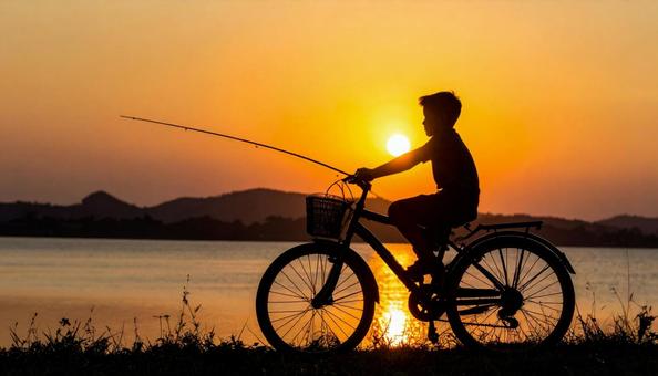 夕日を背景に自転車に乗る釣り少年の写真