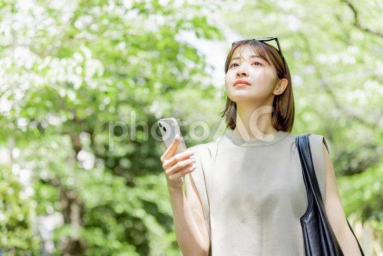 新緑の中、スマートフォンを使う若い女性 女性,外出,お出かけの写真素材