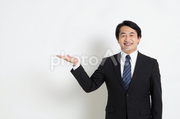 手をあげ笑顔で案内している中年のサラリーマン男性（コピースペース） 中年,上司,会社員の写真素材