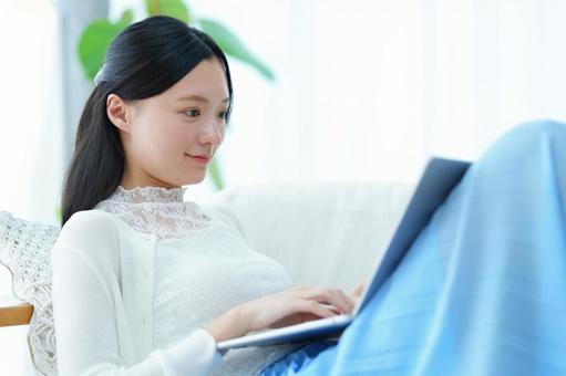 ソファで寛ぎながらパソコン作業をする女性 女性,微笑む,寛ぐの写真素材