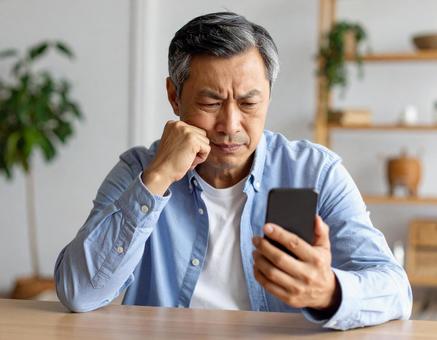 スマートフォンを見ながら考える男性 スマートフォンを見ながら考える男性の写真