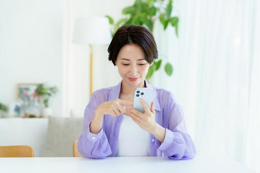 部屋でスマホを操作するミドル女性 部屋でスマホを操作するミドル女性 スマホ,笑顔,女性の写真素材