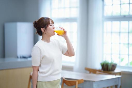 コップでオレンジジュースを飲んでいる女性の写真