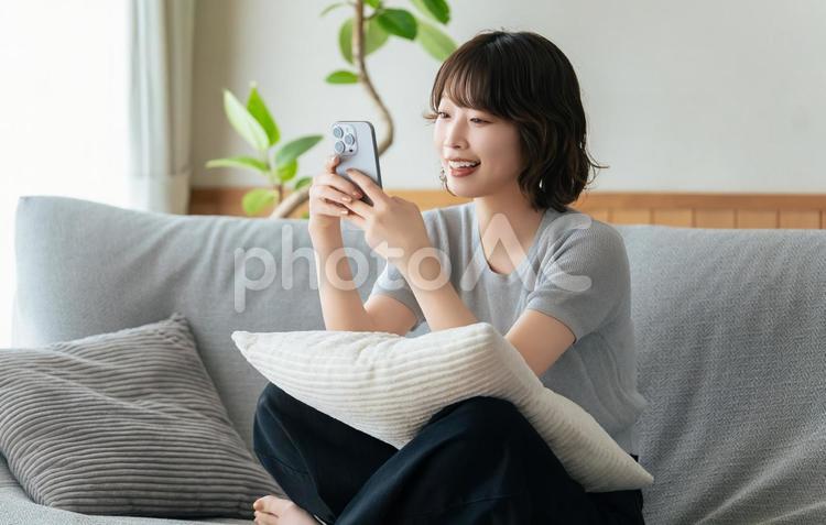 ソファに座ってスマホを使う笑顔の女性 女性,スマホ,スマートフォンの写真素材