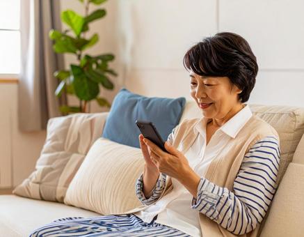 自宅でスマホを操作するシニア女性 自宅でスマホを操作するシニア女性の写真