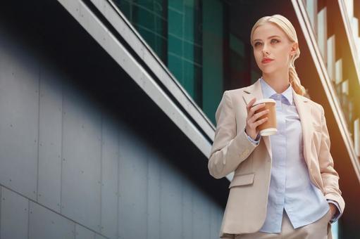 オフィスビルの外でコーヒーを持って立つスーツを着た女性 ビジネスウーマン,ビジネス,女性の写真素材