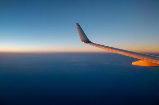 飛行機の窓から見える夕日と海と空と羽 飛行機の窓から見える夕日と海と空と羽の写真