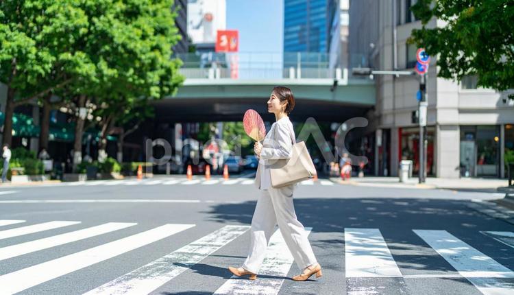 うちわを手に夏の街を歩くビジネスウーマン うちわ,暑い,美しいの写真素材