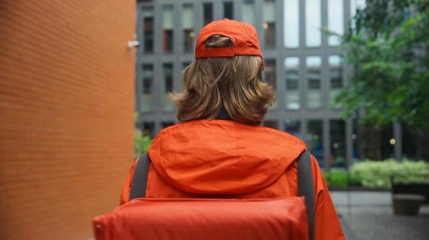 街なかにいる配達バッグを背負ったフードデリバリーの男性の後ろ姿 配達,フードデリバリー,デリバリーの写真素材