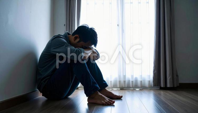薄暗い部屋の床に座り膝に頭を埋める男性 男性,苦悩,落ち込むの写真素材