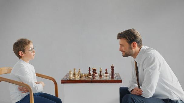 向かい合ってチェスをしている横向きのお父さんと男の子(グレー背景) 向かい合ってチェスをしている横向きのお父さんと男の子(グレー背景) チェス,親子,お父さんの写真素材