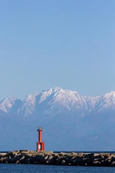 赤い灯台と雪を被った立山連峰_縦の写真