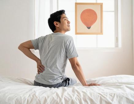 ベットの上で腰を抑えて苦しむ男性 ベットの上で腰を抑えて苦しむ男性の写真