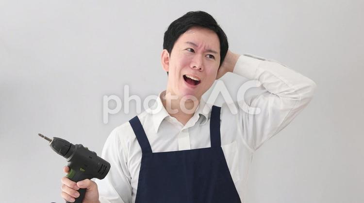 電動ドリルを持ちながら困るエプロンの男性 エプロン,男性,ドリルの写真素材