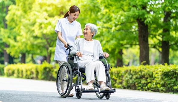 車椅子を押してシニア女性と笑う若い介護士 車椅子を押してシニア女性と笑う若い介護士の写真