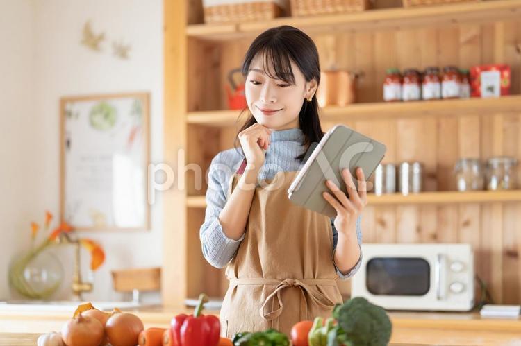 タブレットを見ながら料理をする笑顔の女性 女性,キッチン,料理の写真素材