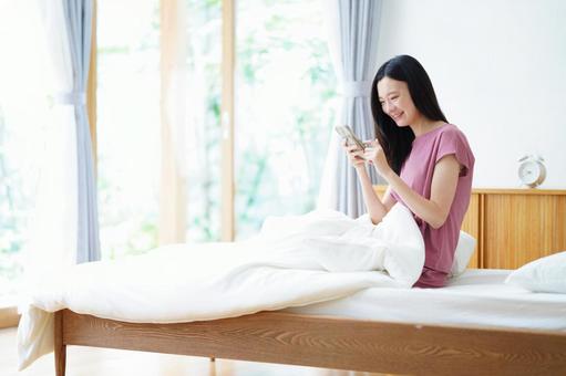 ベッドに座りスマホを持ち笑うロングヘアの女性 女性,スマートフォン,持つの写真素材