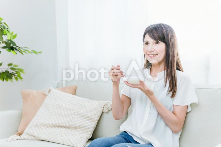 ソファでヨーグルトを食べる女性（笑顔） ヨーグルト,乳酸菌,菌活の写真素材