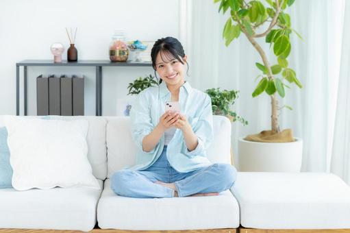 部屋でスマホを操作する若い女性 スマホ,笑顔,女性の写真素材