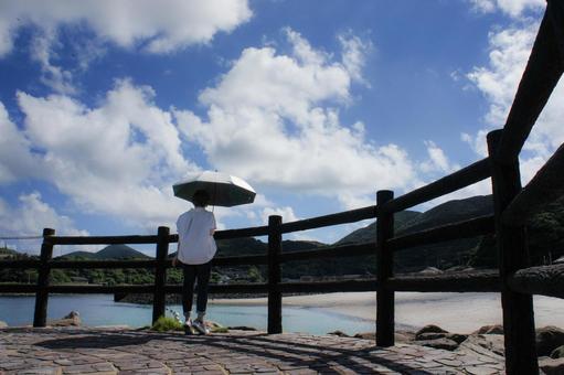 <素材>海辺の遊歩道を散歩する日傘の女性 <素材>海辺の遊歩道を散歩する日傘の女性の写真