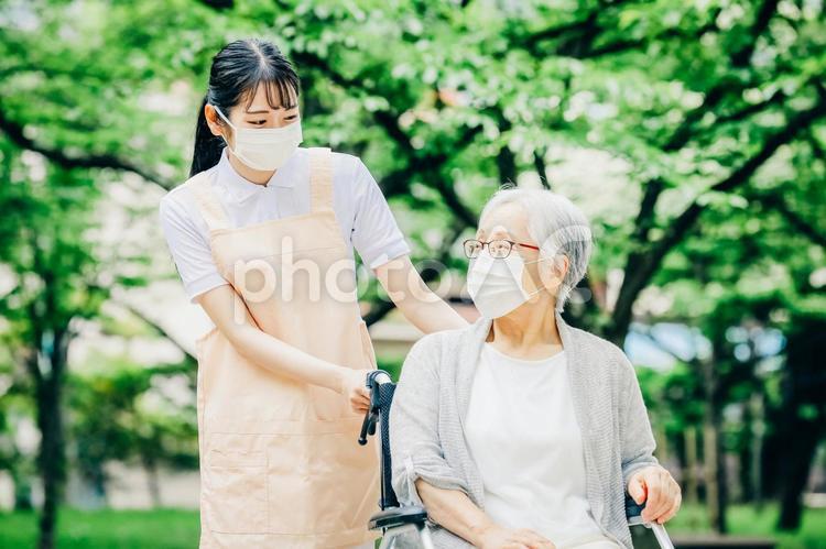車椅子に乗った高齢者女性と女性スタッフ（マスク） 介護,老人ホーム,看護師の写真素材