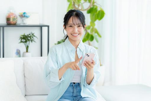部屋でスマホを操作する若い女性 スマホ,笑顔,女性の写真素材