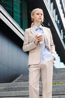 オフィスビルの外でコーヒーを持って立つ女性 ビジネスウーマン,ビジネス,女性の写真素材