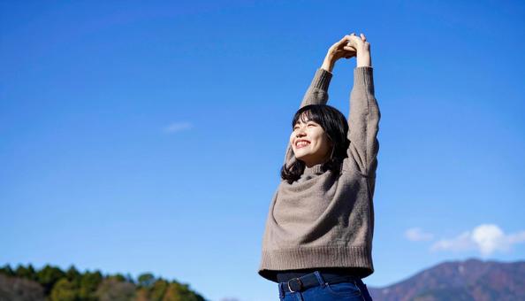 青空の下で伸びをする秋服の日本人女性 青空の下で伸びをする秋服の日本人女性の写真