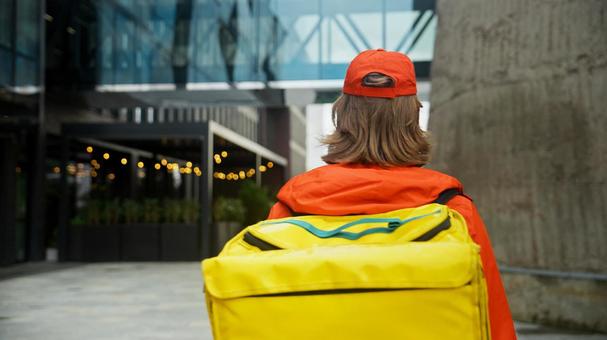 街なかにいる配達バッグを背負っているフードデリバリーの男性の後ろ姿 配達,フードデリバリー,デリバリーの写真素材