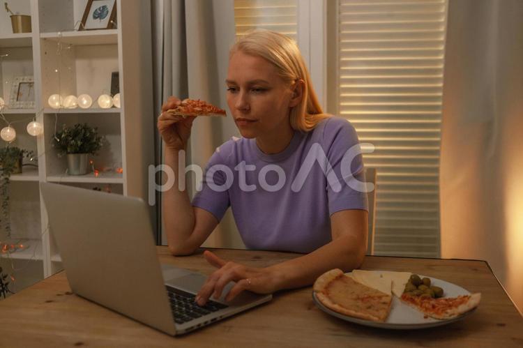 ピザを持ちながらパソコンを見ている女性 女性,ピザ,持つの写真素材