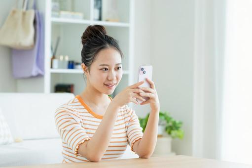 リビングでスマホを見る若い女性 リビングでスマホを見る若い女性の写真
