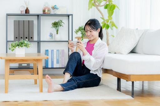 部屋でスマホを操作する若い女性 スマホ,笑顔,若い女性の写真素材