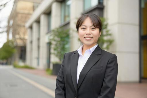 ビル街でカメラ目線のスーツの女性 ビル街でカメラ目線のスーツの女性 日本人,女性,20代の写真素材