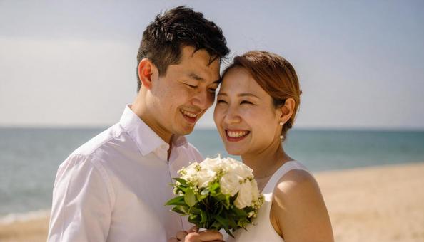 海辺でブーケを持ち顔を見合わせる新郎新婦 海辺でブーケを持ち顔を見合わせる新郎新婦の写真