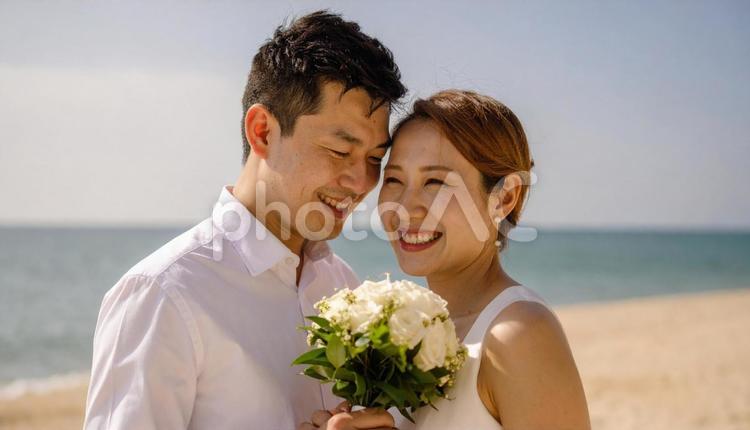 海辺でブーケを持ち顔を見合わせる新郎新婦 海,ウエディング,結婚の写真素材