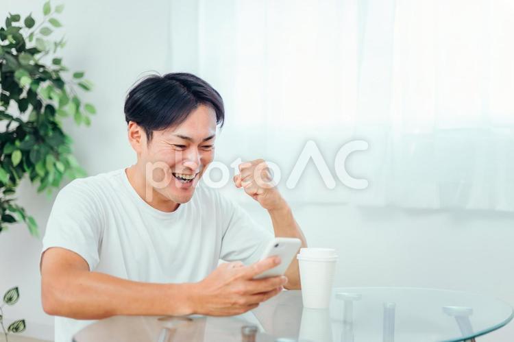 部屋でスマホを見る男性（ガッツポーズ） スマホ,スマートフォン,アプリの写真素材