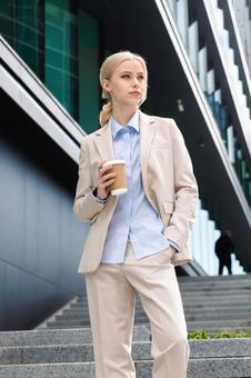 オフィスビルの外に居るコーヒーを持った女性 ビジネスウーマン,ビジネス,女性の写真素材